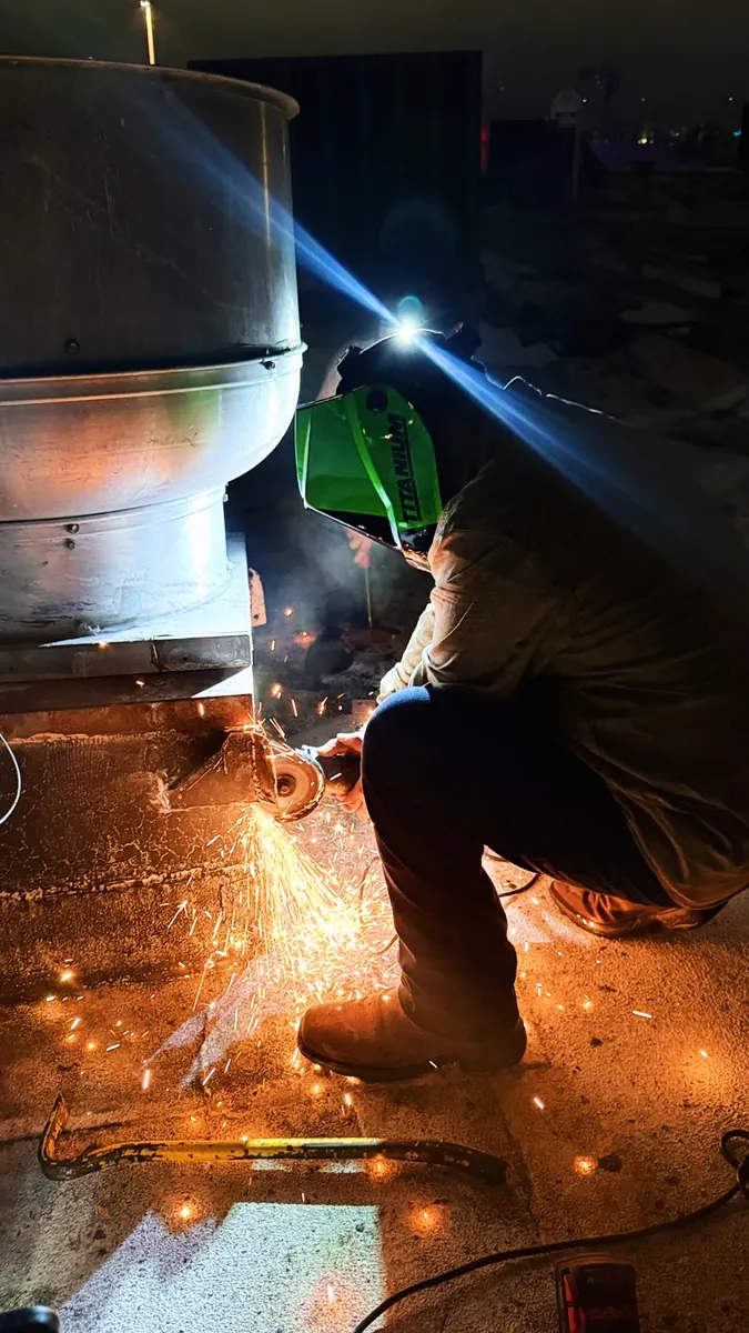 Grease Monsters technician servicing a rooftop exhaust fan at night